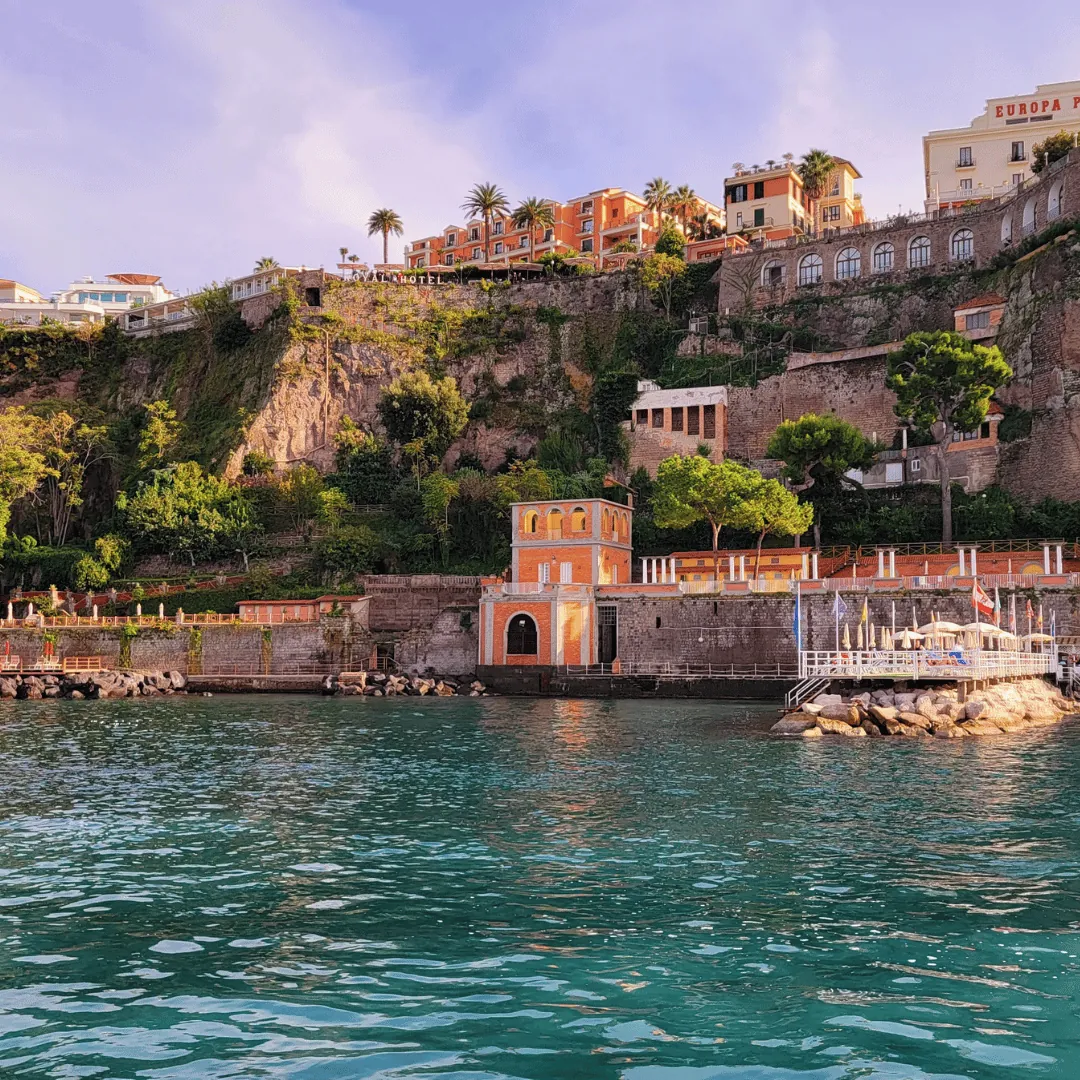 Le scogliere di Sorrento con palme ed edifici color pastello viste dal mare turchese
