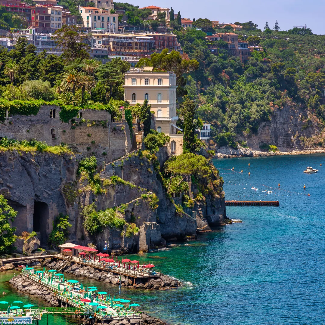 Costa di Sorrento con una villa sulla scogliera di tufo e i pontili sul mare turchese
