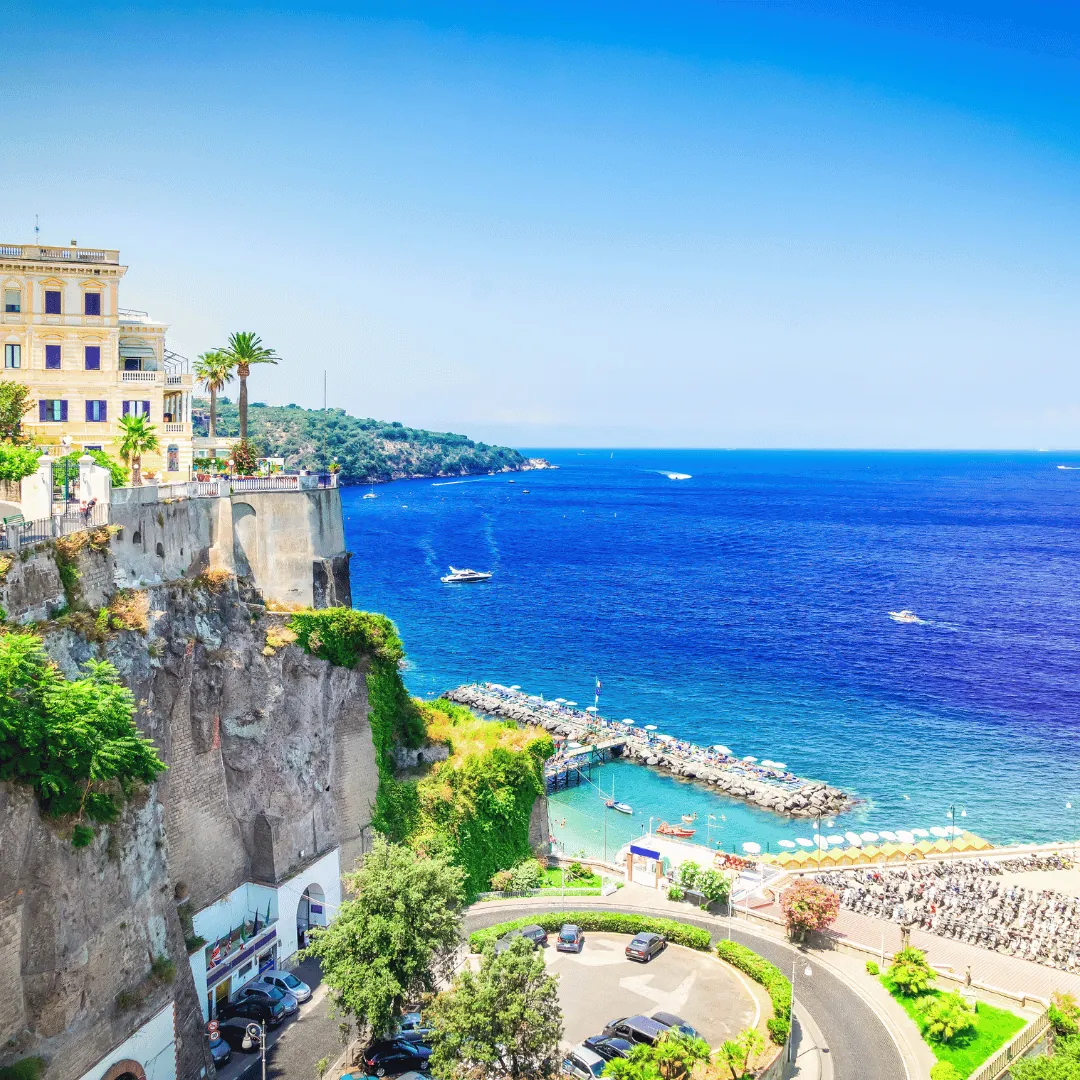 Marina Piccola di Sorrento vista dall'alto della scogliera, con i pontili sul mare blu e la strada che scende al porto